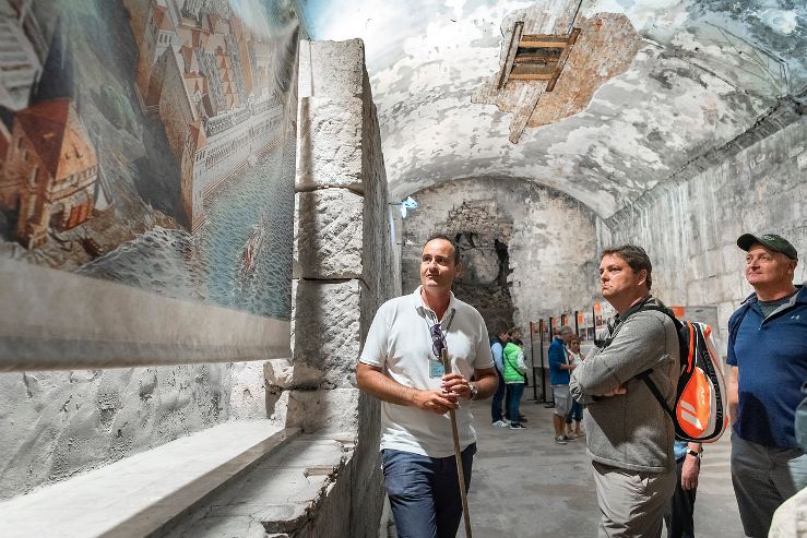 A guide talking to a small group of guests in a vaulted stone hall