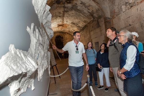 A guide showing guests a white relief model inside a stone vault